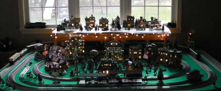 A holiday train layout with an illuminated village and carnival scenery